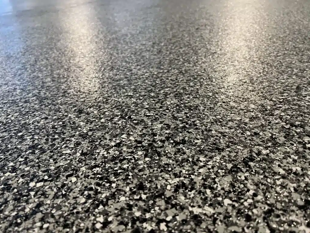 The image shows a close-up view of a speckled, shiny floor surface with a granular texture reflecting some light, likely an interior setting.