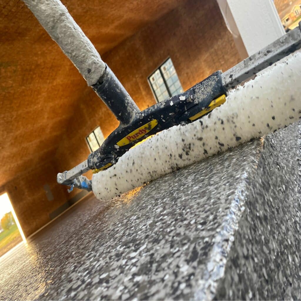 This image shows a close-up, low-angle view of a skateboard on textured ground, with speckled steps leading upward and an illuminated building in the background.