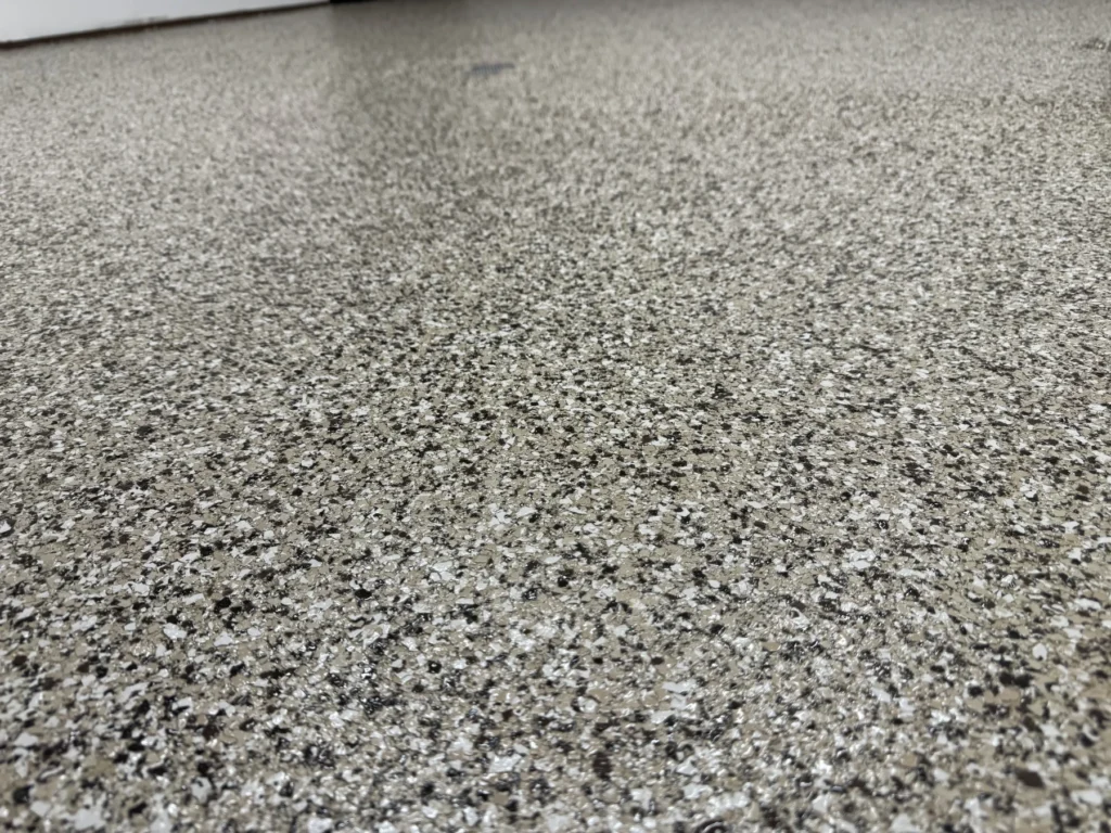 A close-up view of a speckled, textured floor surface composed of various shades of gray and black, creating a polished, durable appearance.