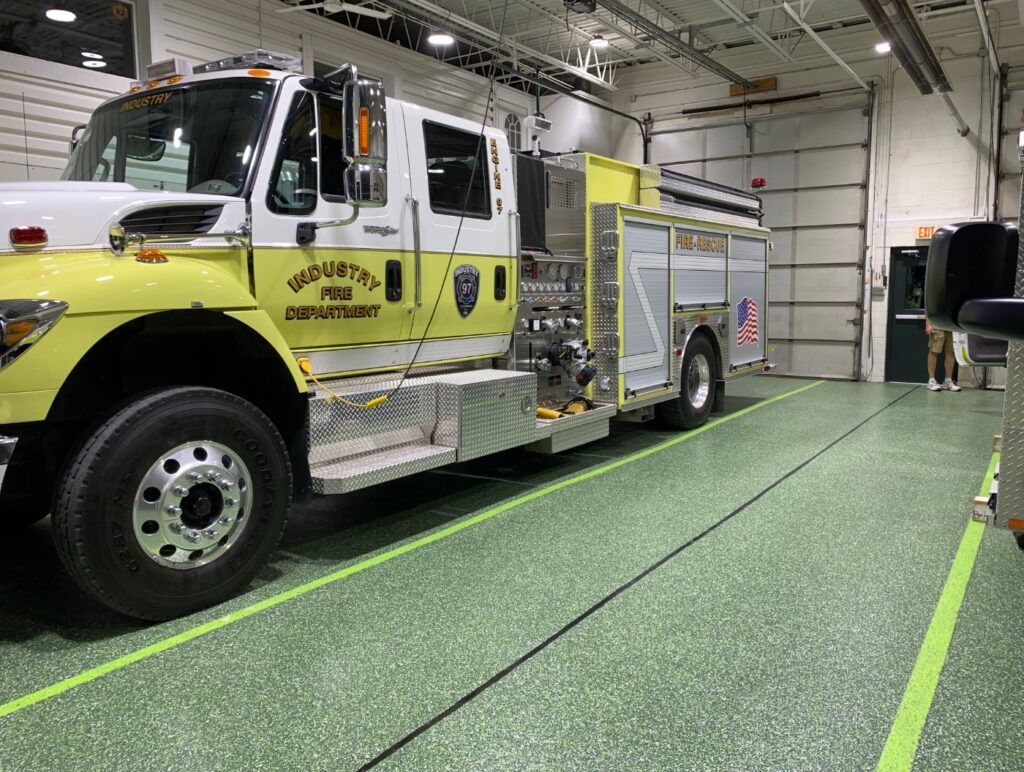 A fire truck with "Industry Fire Department" parked in a station. A person stands near a door in the background.