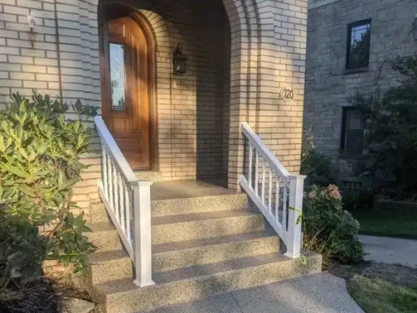 This image shows the entrance to a residential building featuring a beige brick archway, a wooden door, white railings, steps, and house number "720."