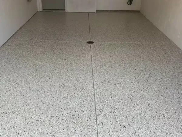 This image shows a clean, epoxy-coated garage floor with a drain, a water hose and spigot on the wall, and subtle gray speckling.