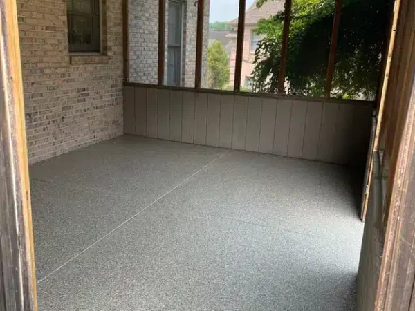 This is an empty screened porch with a speckled floor, brick walls, large windows, and a wooden ceiling viewed from an open doorway.