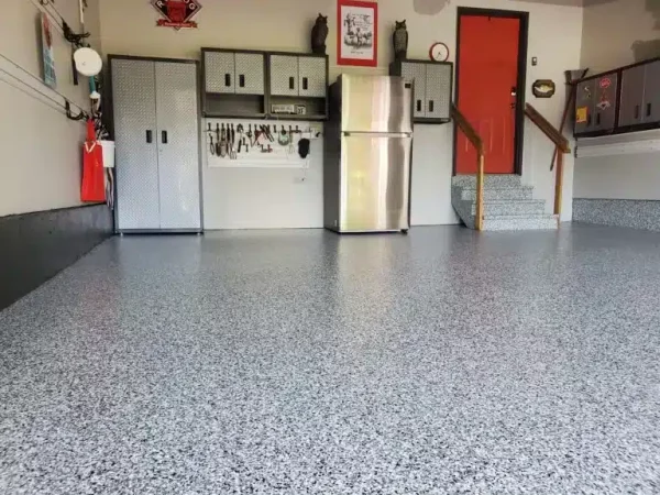 The image shows a tidy garage interior with a speckled floor, metal cabinets, a refrigerator, and an orange door. Tools are organized on the wall.