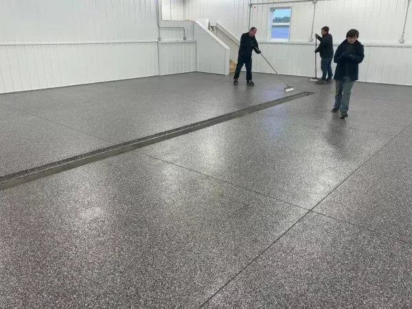 The image shows three people inside a room with a shiny, speckled floor. One person is pushing a wide broom or mop across the floor.