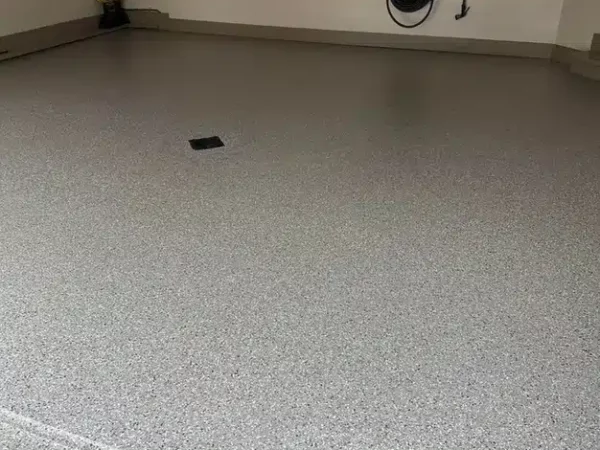 This image shows a tidy garage with a clean, speckled floor. Shelves with organized items and a coiled hose are visible on the back wall.