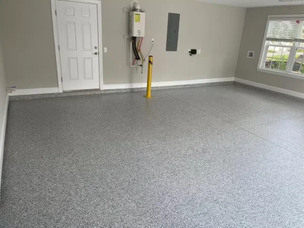 This is an image of a spacious room with a speckled epoxy floor coating, light gray walls, a white door, and a window to the outside.