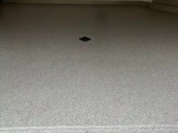 This image shows a clean, speckled garage floor with a central drain, hose reel on the wall, and organized tools hanging neatly on the left.